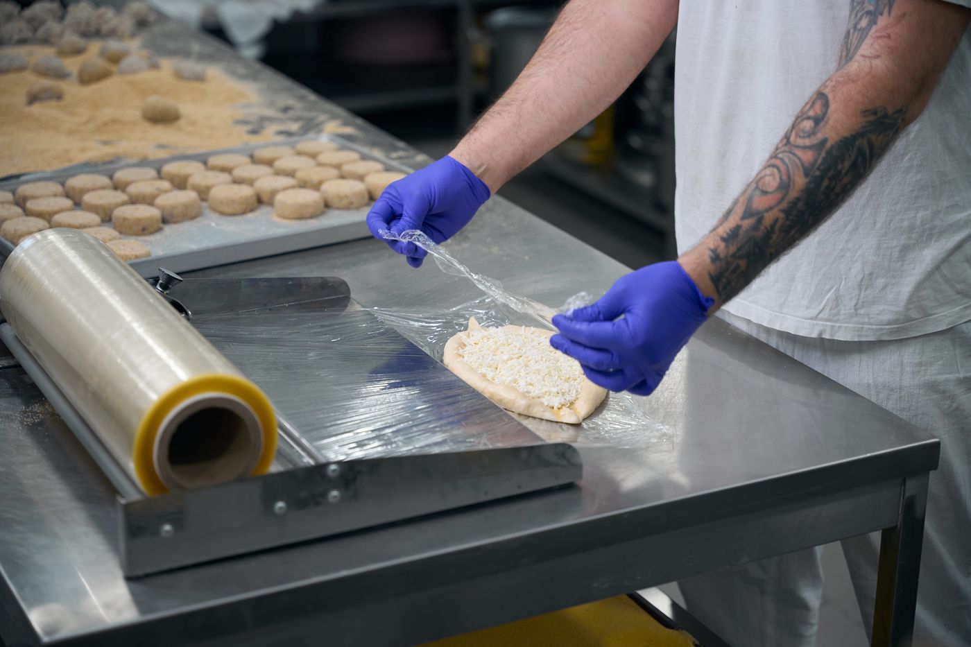 Food production worker wrapping dough with cling film